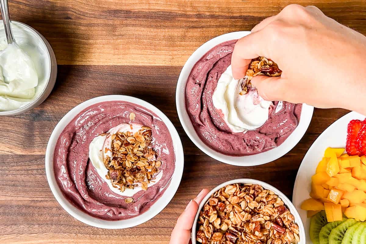 Adding the acai base to white bowls along with yogurt and granola.