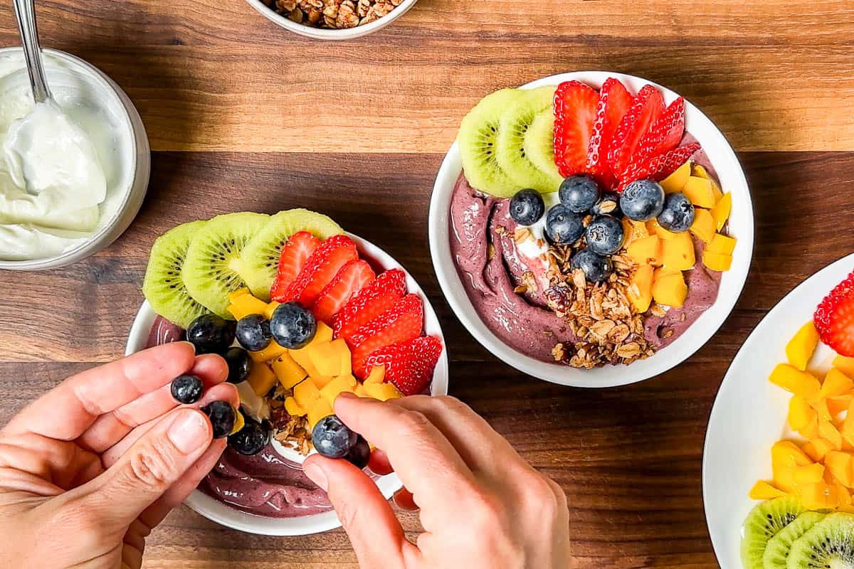 Topping the acai bowls with fresh sliced kiwi, strawberries and bluberries.