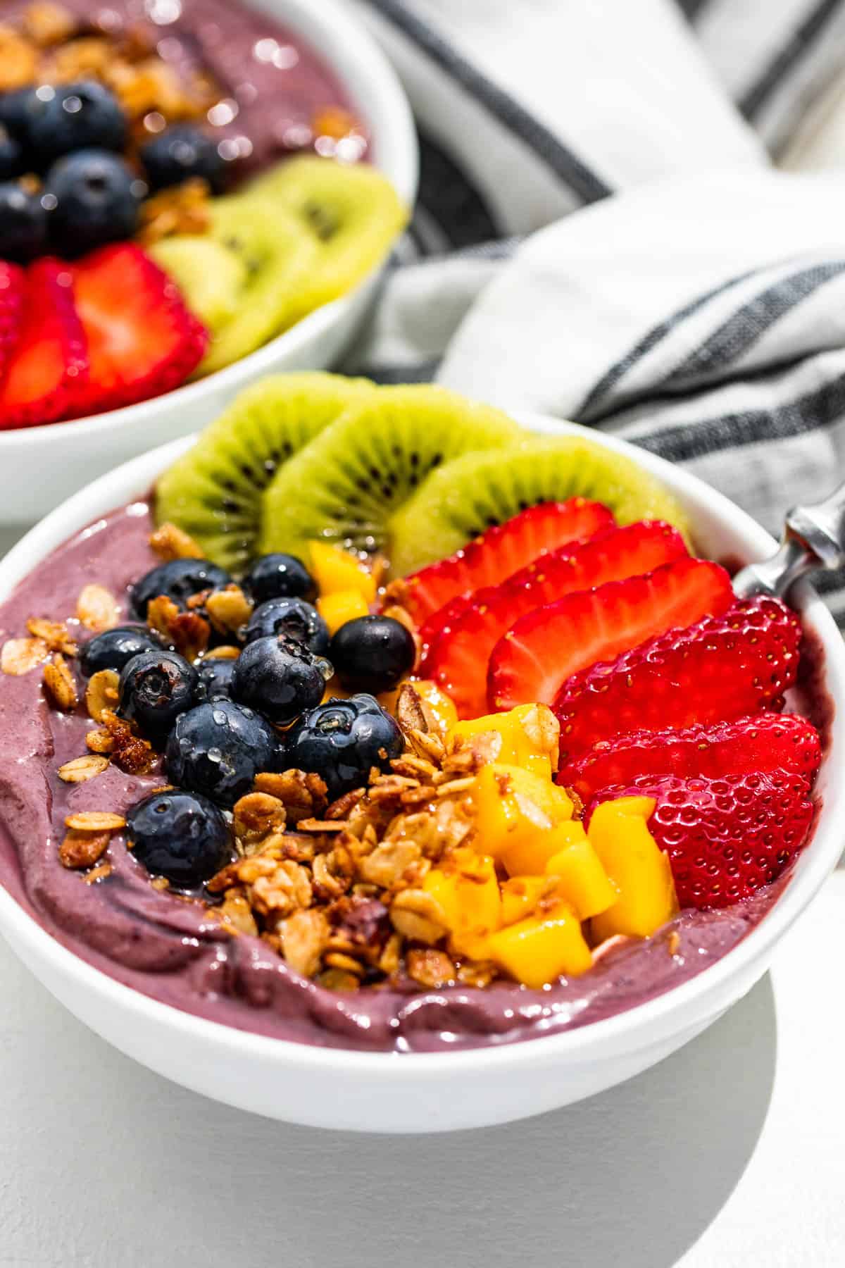 Close up side view of Acai Bowls on a white background with a blue and white striped linen.