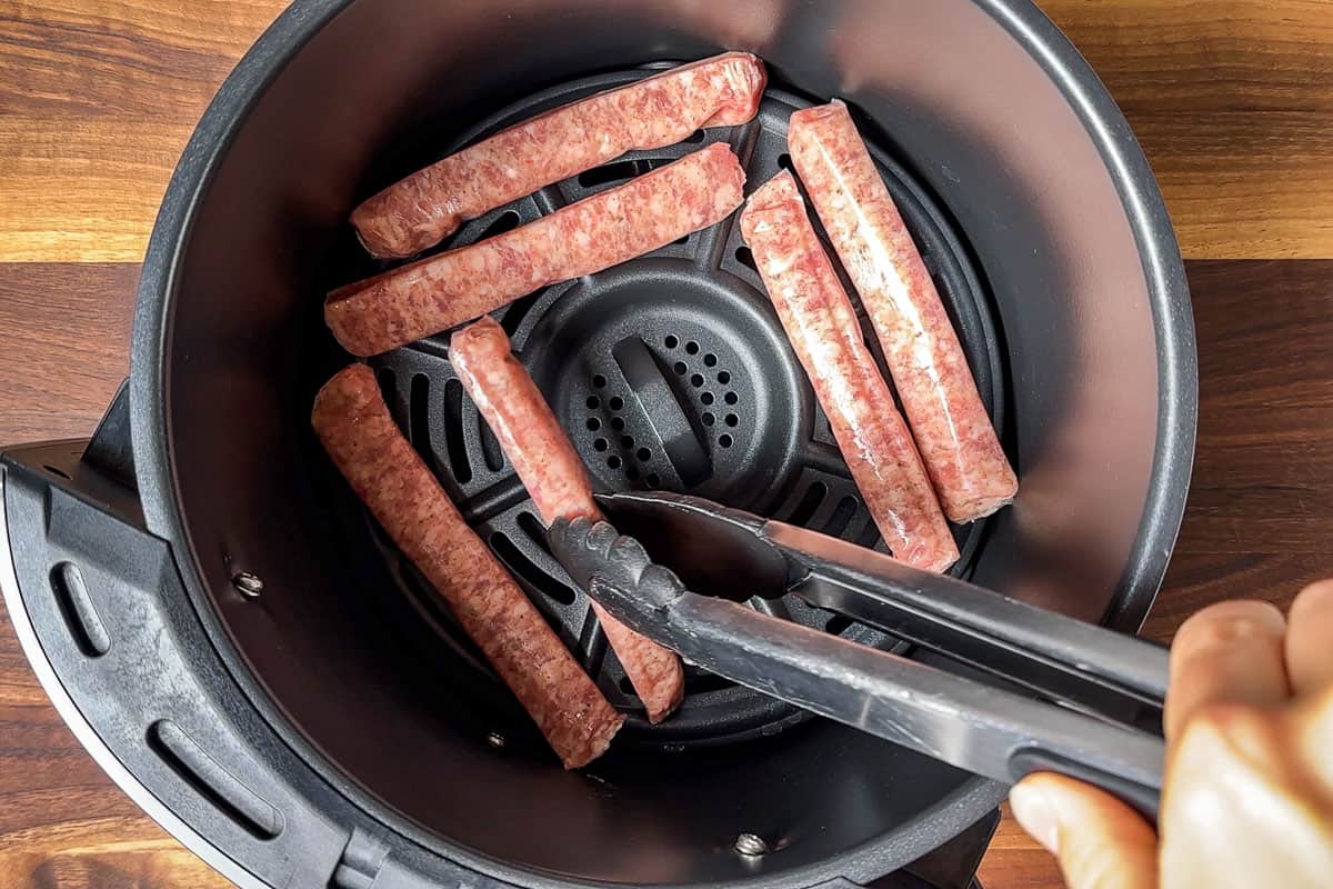 Placing the breakfast sausage links into the air fryer basket with tongs.