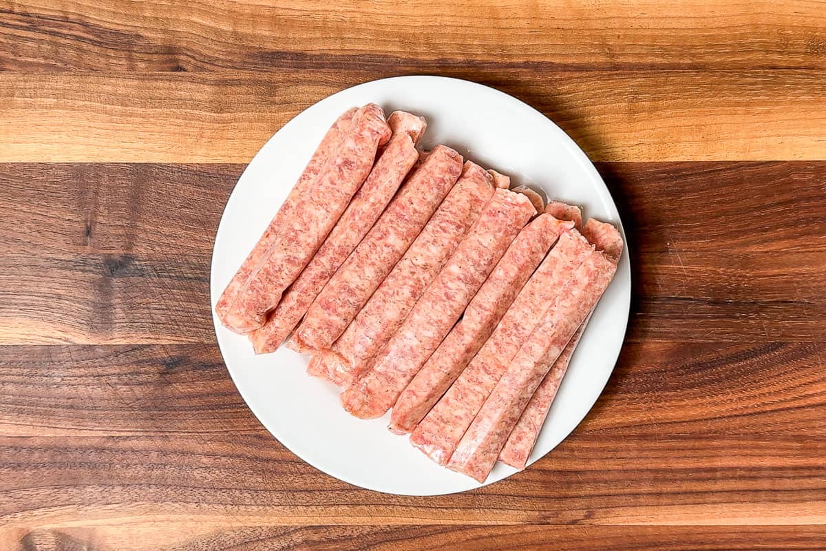 Small breakfast sausage links on a white plate on a wood cutting board.