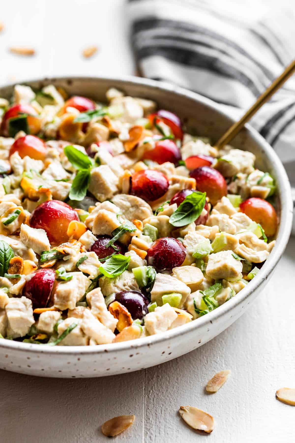 Chicken Salad in a speckled pottery bowl with a gold serving spoon and a blue and white linen behind the bowl.