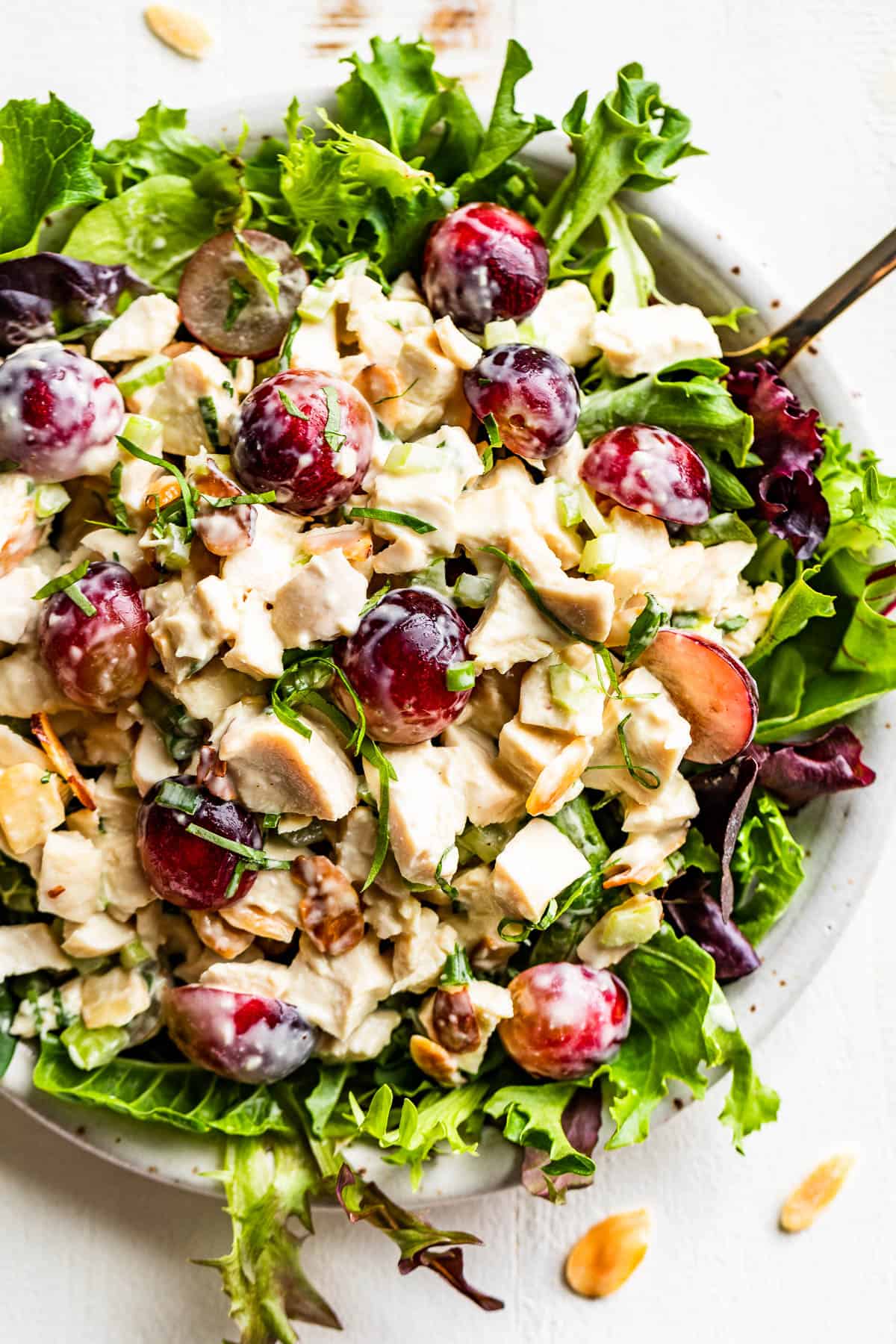 Chicken salad on a bed of spring greens with a gold fork and slice almonds sprinkled around.