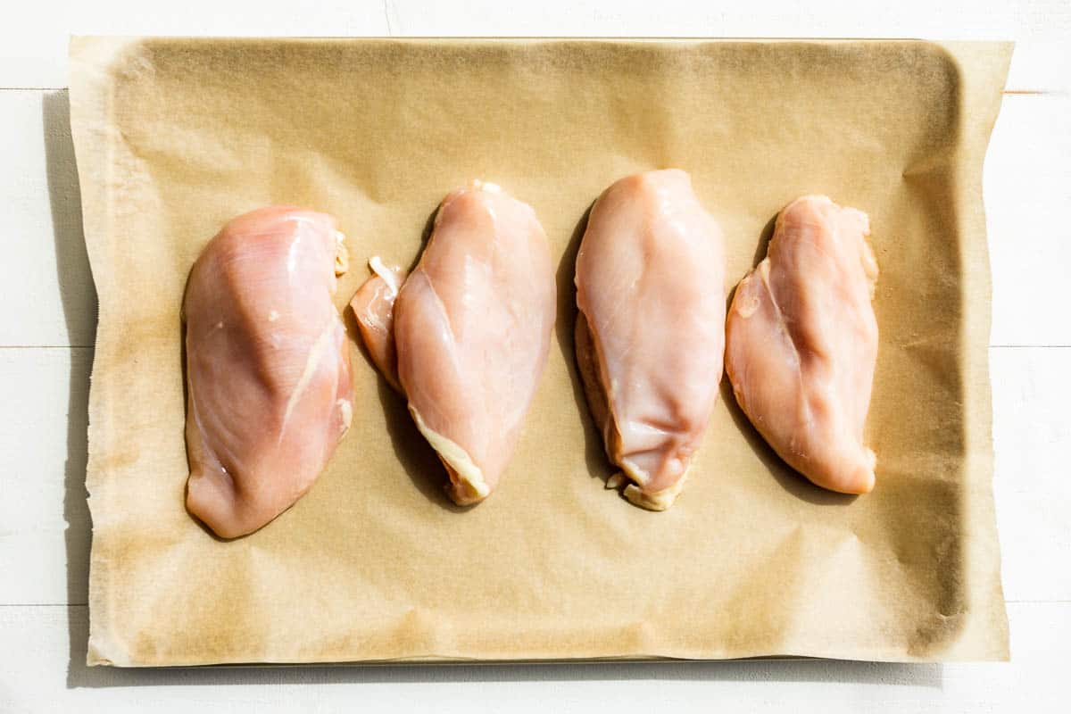 Chicken breasts on a parchment lined baking sheet.