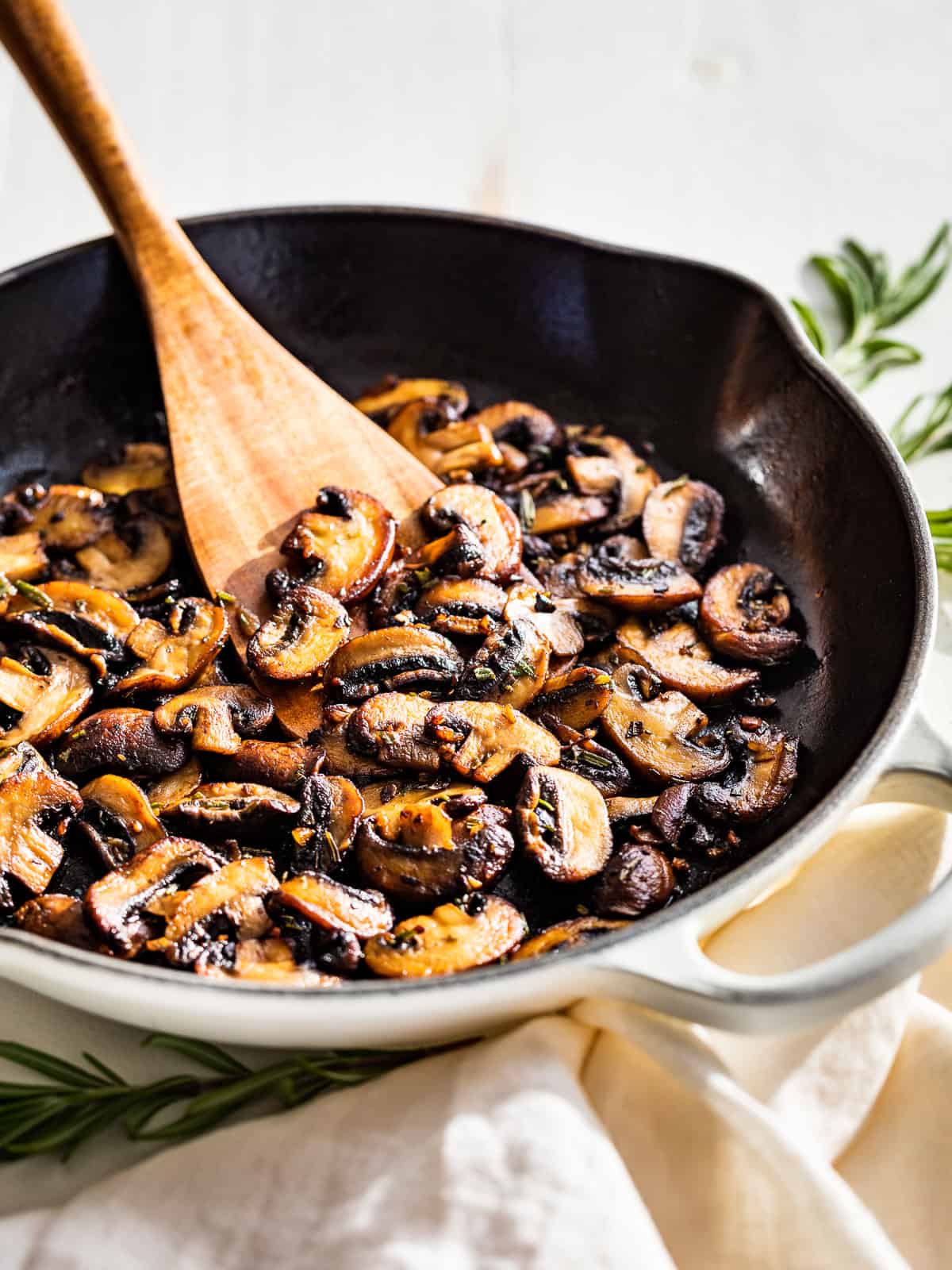 Side view of garlic butter mushrooms in a white skillet with a wood spatula scooping some out.