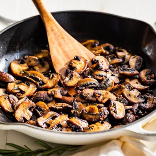 Finished Garlic Butter Mushrooms in a white skillet with rosemary sprigs on the side.