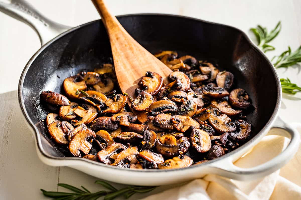 Finished Garlic Butter Mushrooms in a white skillet with rosemary sprigs on the side.