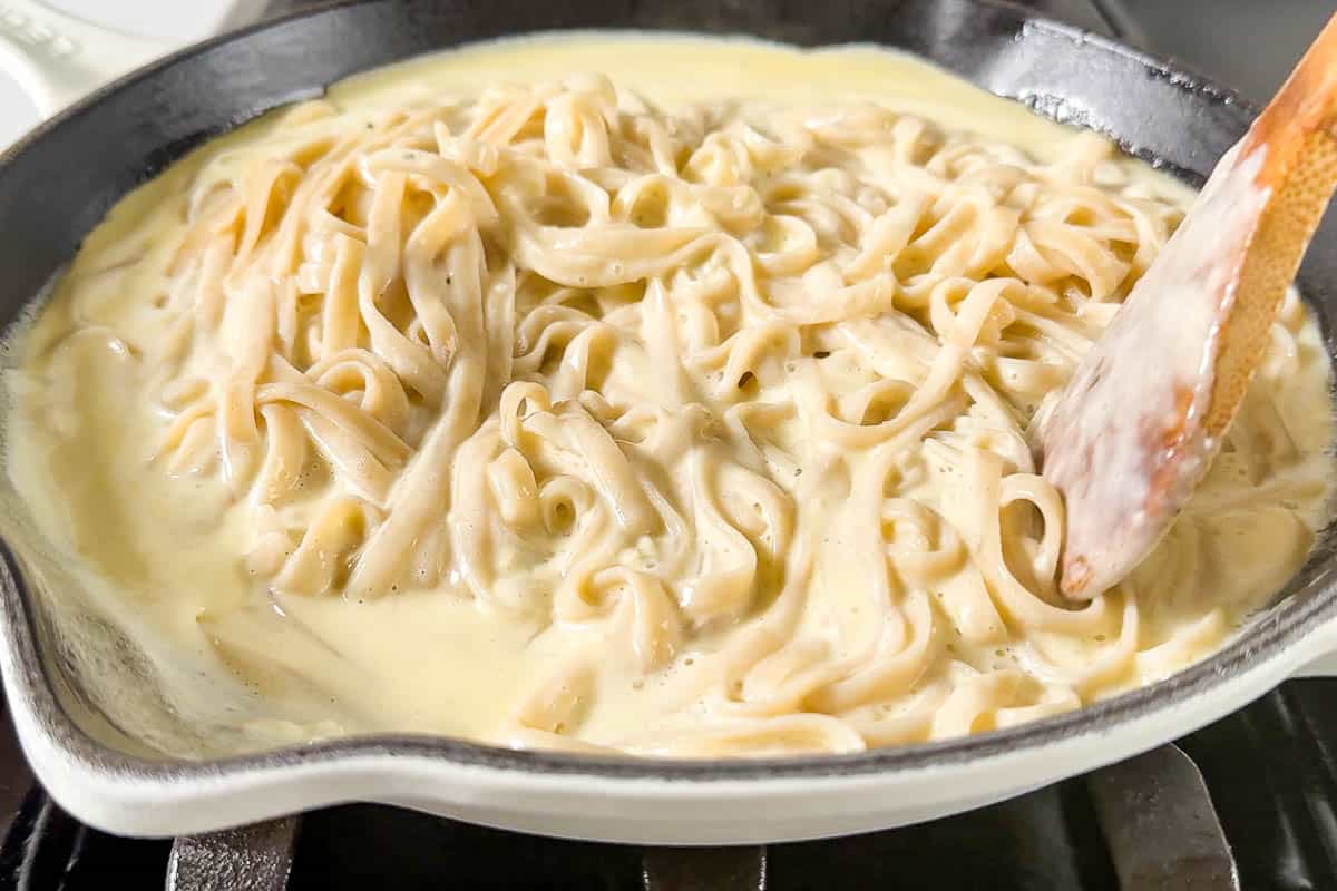 Tossing the freshly cooked Fettuccini together with the Garlic Parmesan Cream. Sauce in a large white skillet with tongs.