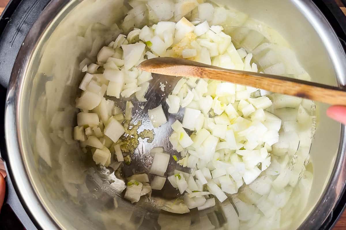 Sautéing the diced onion and garlic in an Instant Pot with a wood spoon.