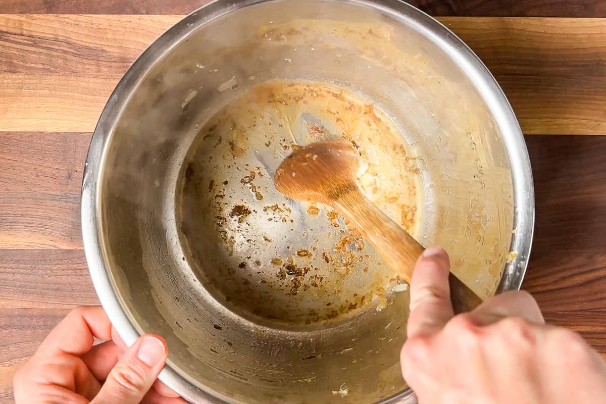 Scraping up the browned bits with a bit of chicken broth from the bottom of the Instant Pot with a wood spoon.