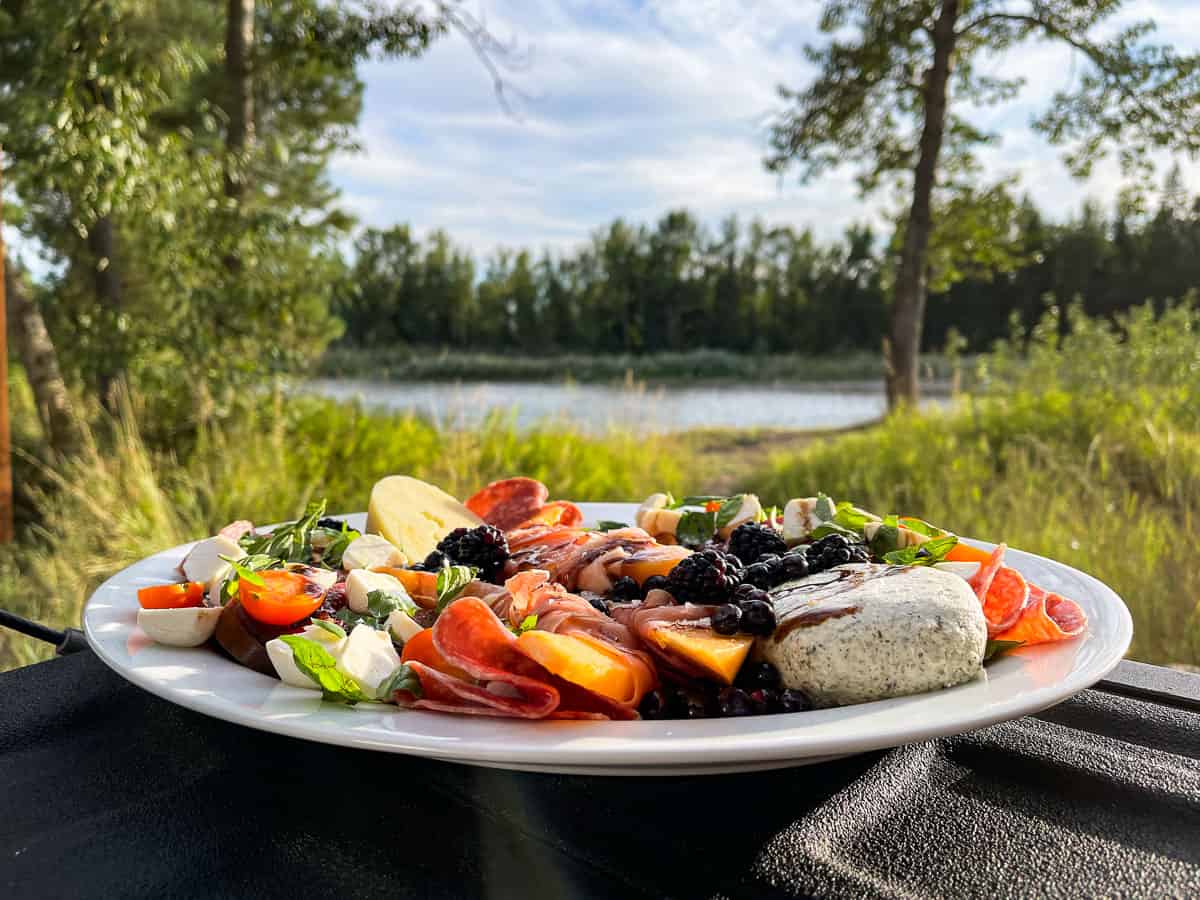 Summer Antipasto Platter sitting on a truck tailgate with trees and a river in the background.