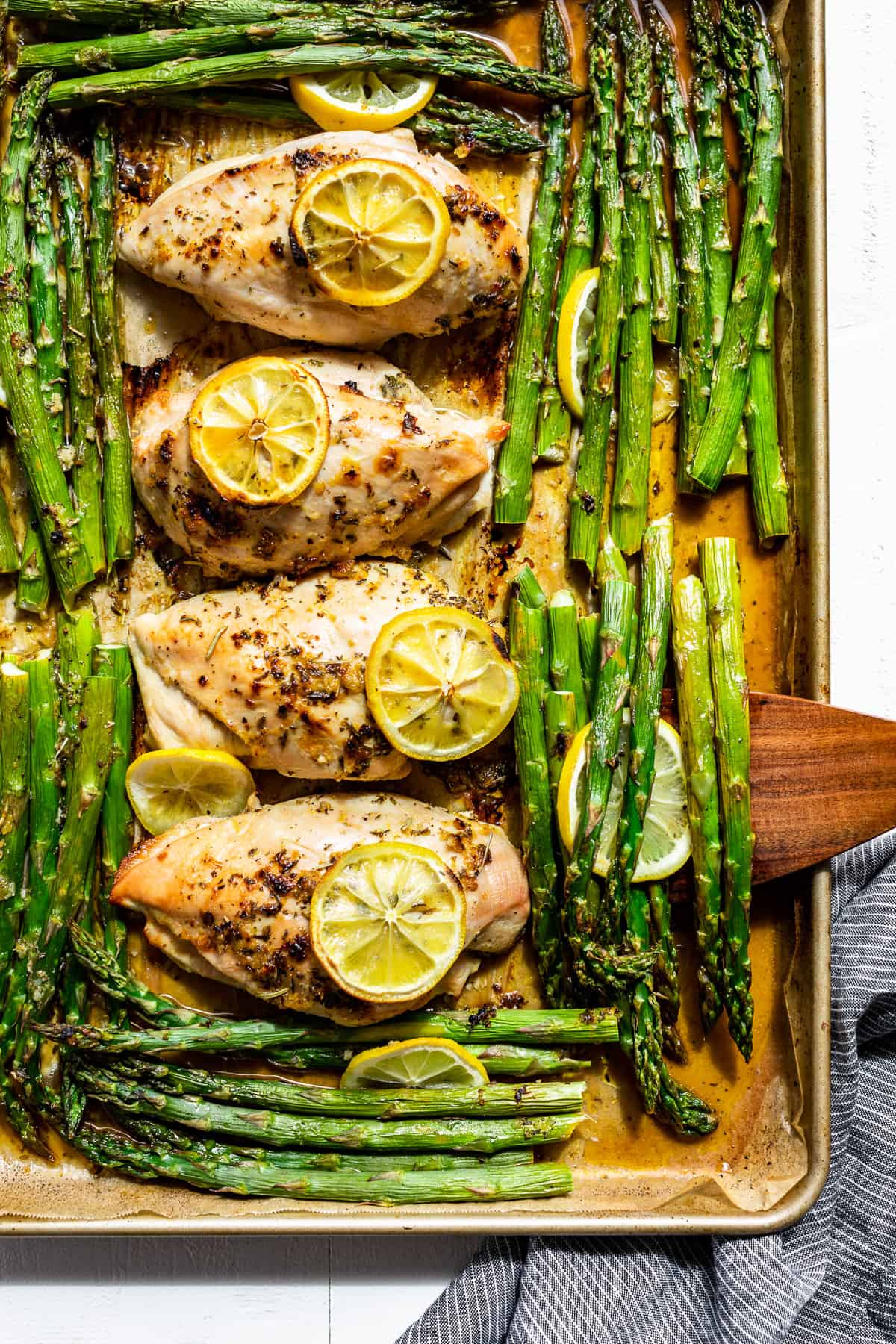 Lemon Chicken and asparagus on a sheet pan with a wood spatula scooping some out.