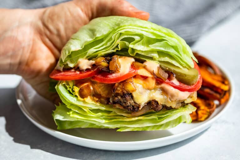 A hand holding a Burger Lettuce Wraps with sweet potato fries on a white plate.