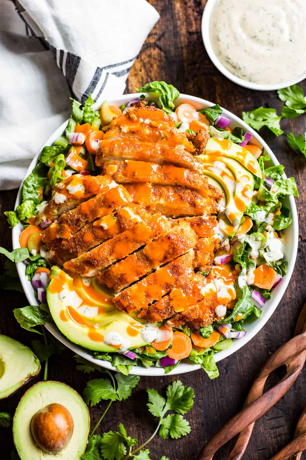 Crispy Buffalo Chicken Salad in a white bowl with an avocado and ranch dressing on the side.