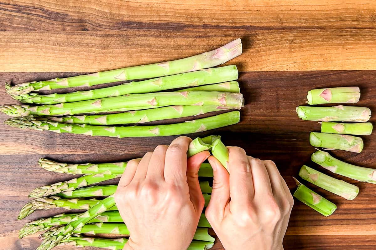 Snapping off the ends of the asparagus on a wood cutting board.