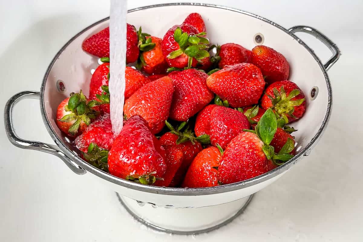 Washing fresh strawberries in a white colander in a white sink.