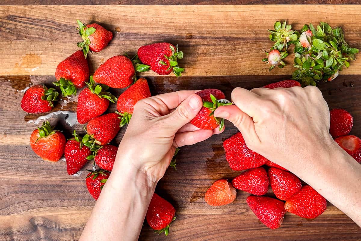 Hulling the fresh strawberries on a wood cutting board.