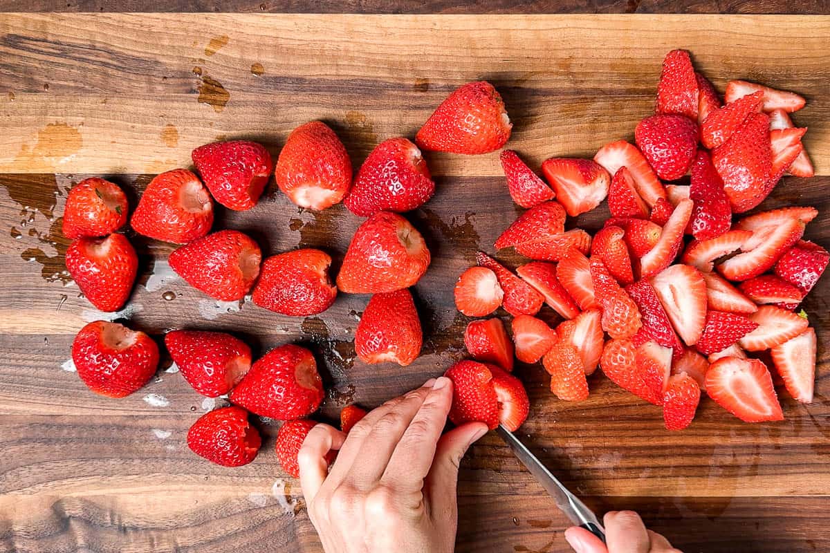 Cutting the hulled strawberries into quarters on a wood cutting board with a pairing knife.