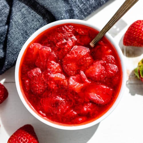 Straight down view of Strawberry Compote in a white bowl with strawberries and a blue linen on the side.