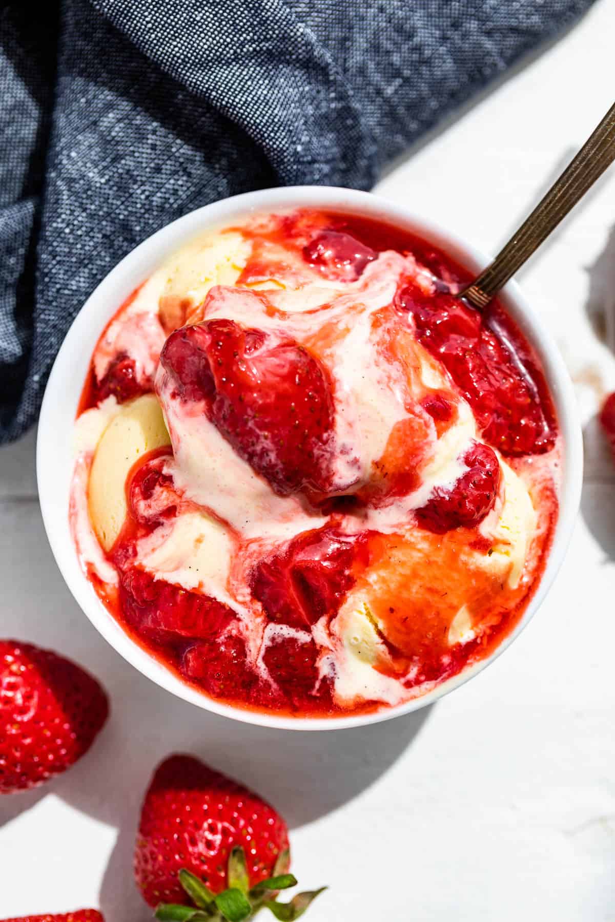 Straight down view of a white bowl of vanilla ice cream topped with Strawberry Compote with strawberries on the side.