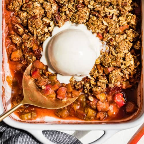 A straight down view of Strawberry Rhubarb Crisp in a white baking dish with a large scoop of coconut ice cream on top.