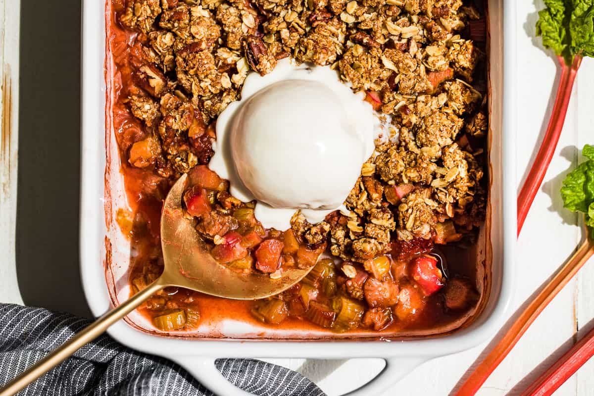 A straight down view of Strawberry Rhubarb Crisp in a white baking dish with a large scoop of coconut ice cream on top.