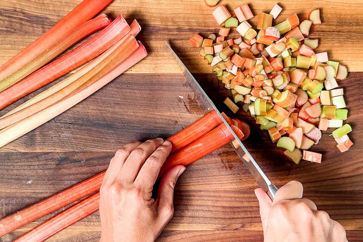 Slicing up the stalks of pink rhubarb on a wood cutting board.