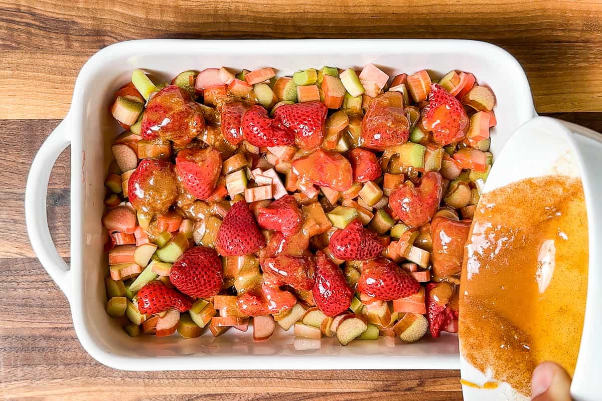 Pouring the maple orange mixture over the sliced rhubarb and strawberries in a baking dish.