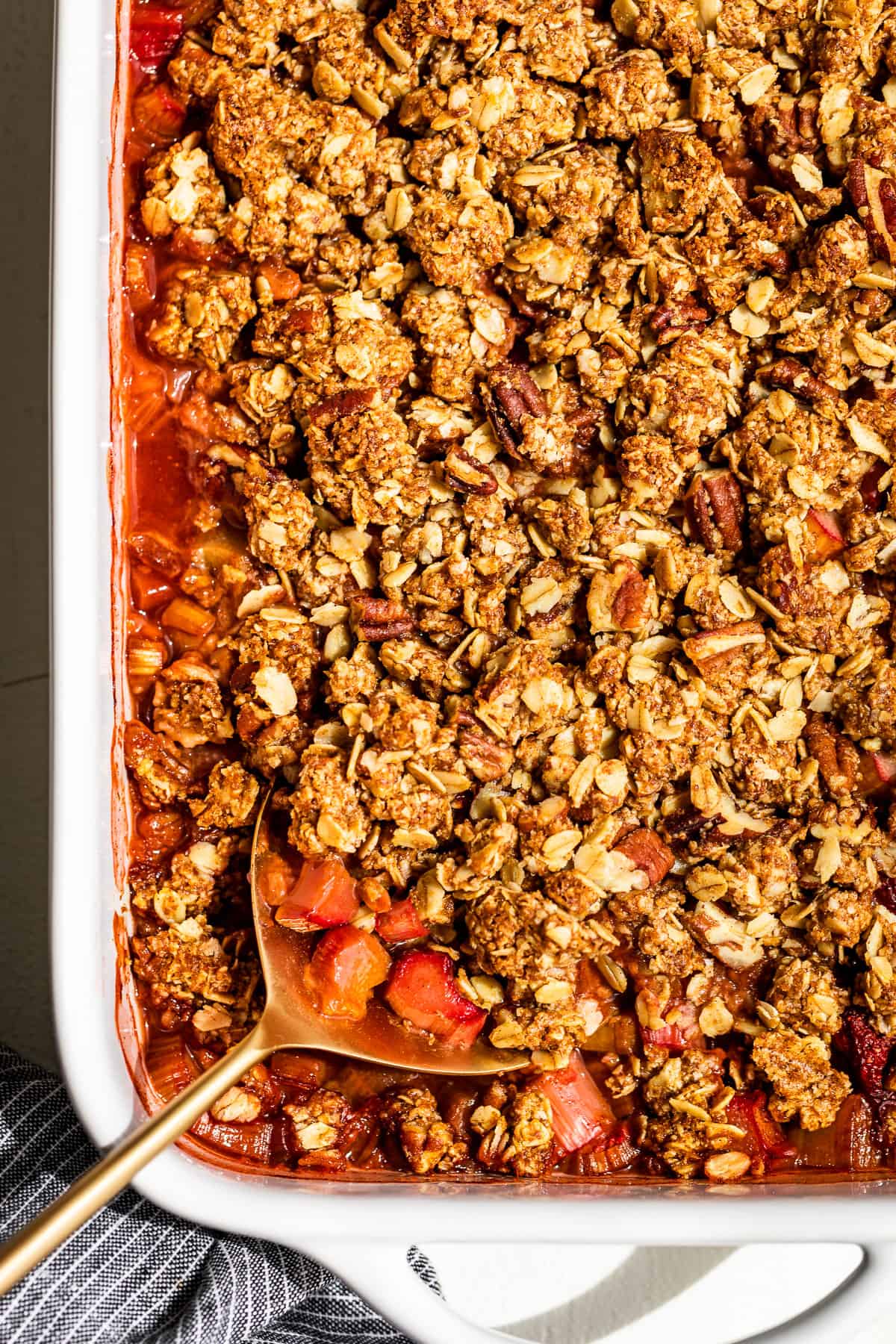 The finished Strawberry Rhubarb Crisp in a white baking dish with a gold serving spoon.
