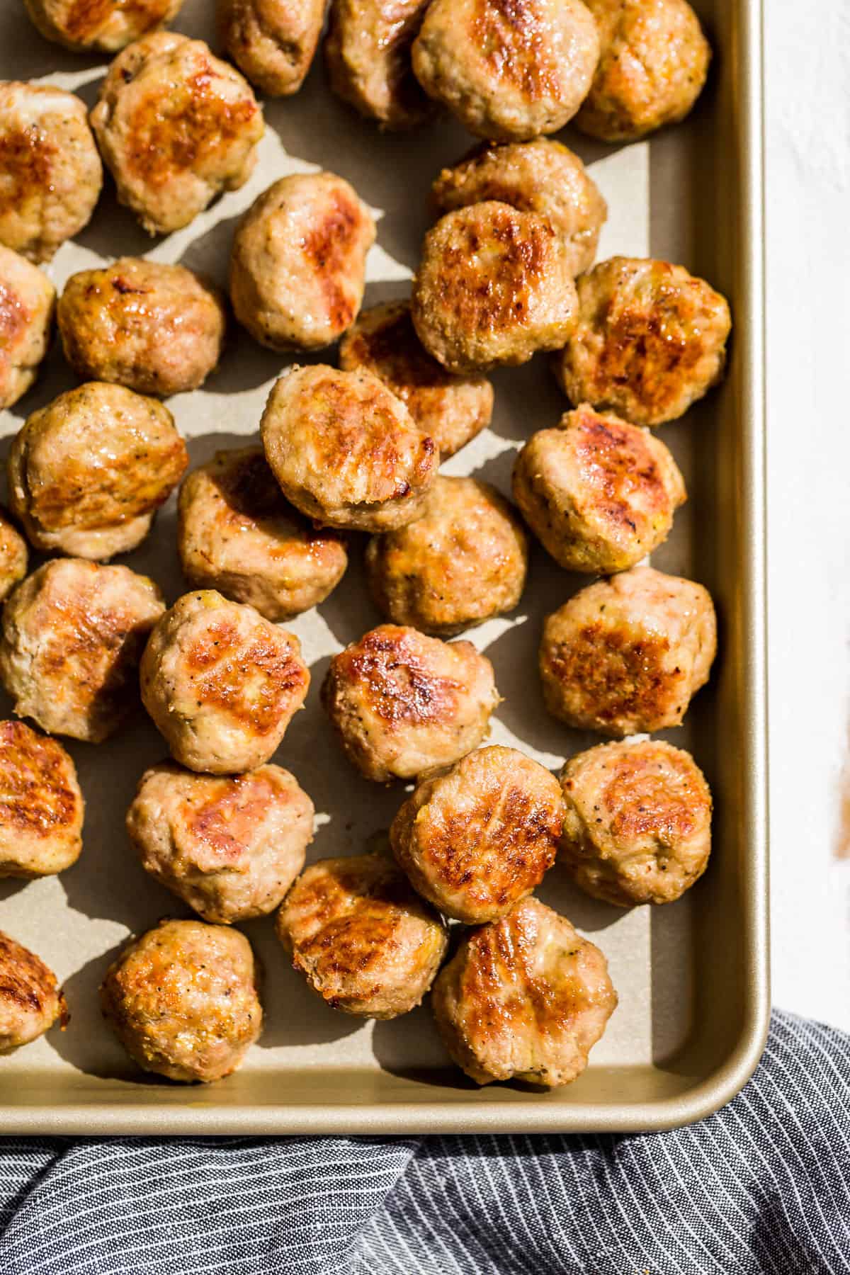 Straight down view of Baked Turkey Meatballs on a gold baking sheet with a blue linen on the side.