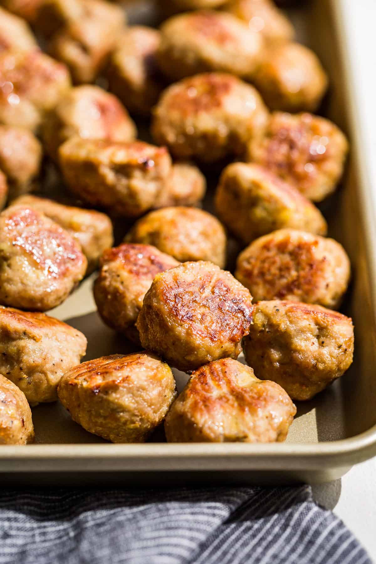 Side view of Baked Turkey Meatballs on a gold baking sheet with a blue linen on the side.