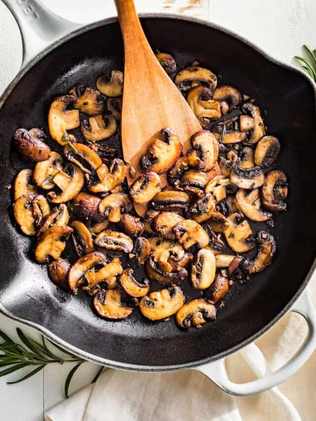 Straight down view of Garlic Butter Mushrooms in a white skillet with a wood spatula scooping some out.