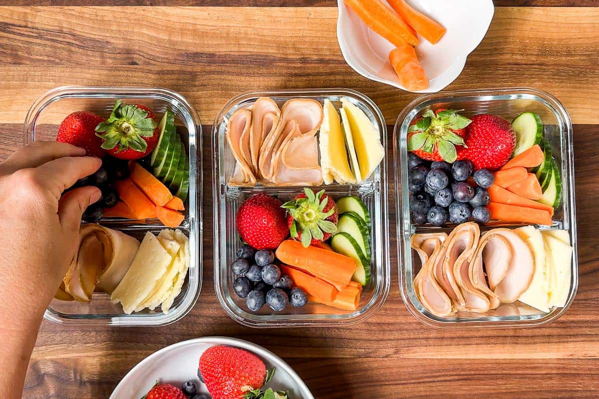 Adding blueberries to the adult lunchables containers on a wood cutting board.