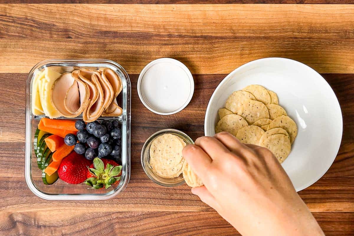 Placing crackers into a separate container next to the finished adult lunchables.