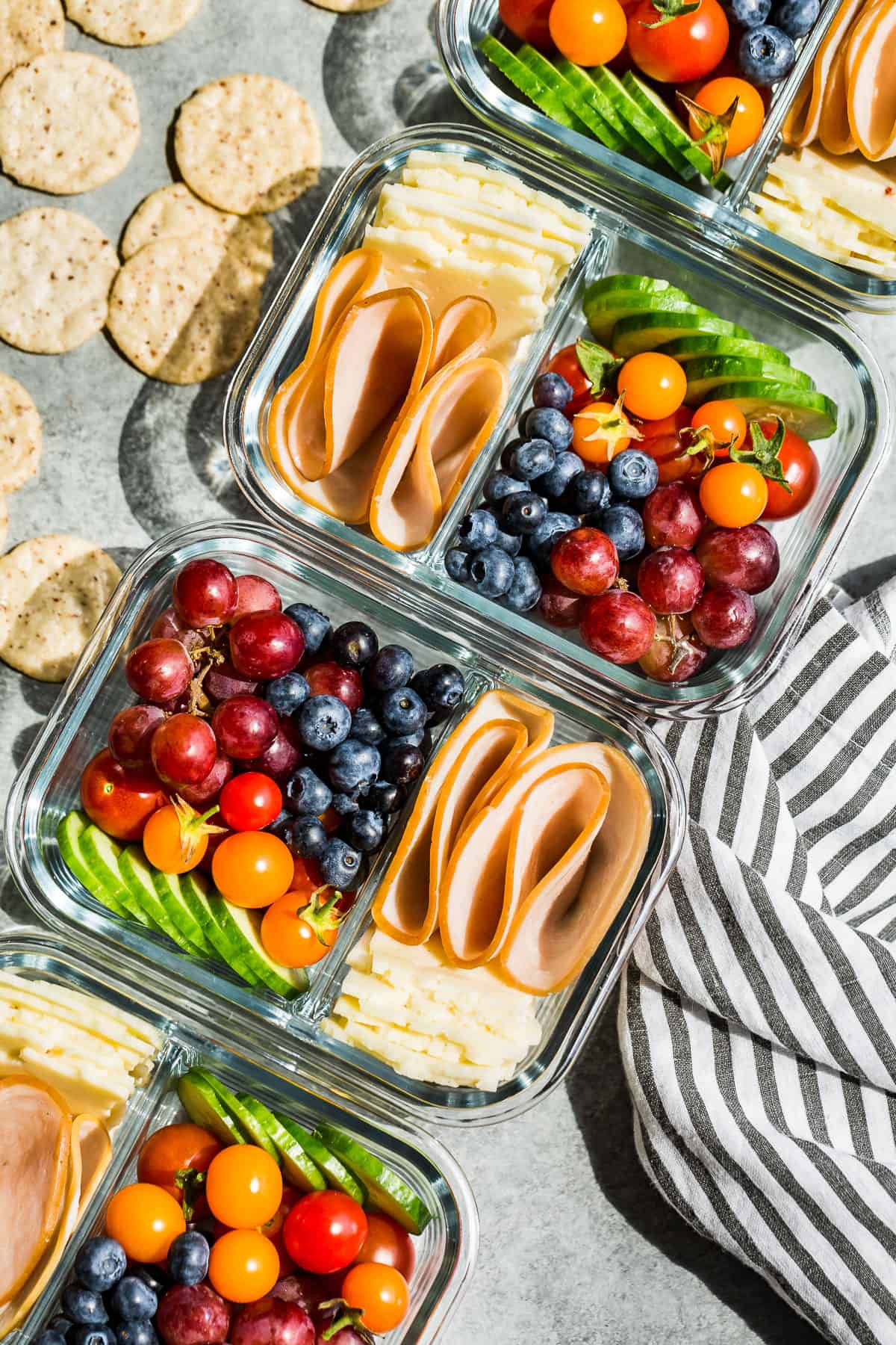 Straight down view of Adult Lunchables in four glass meal prep containers with crackers on the side.