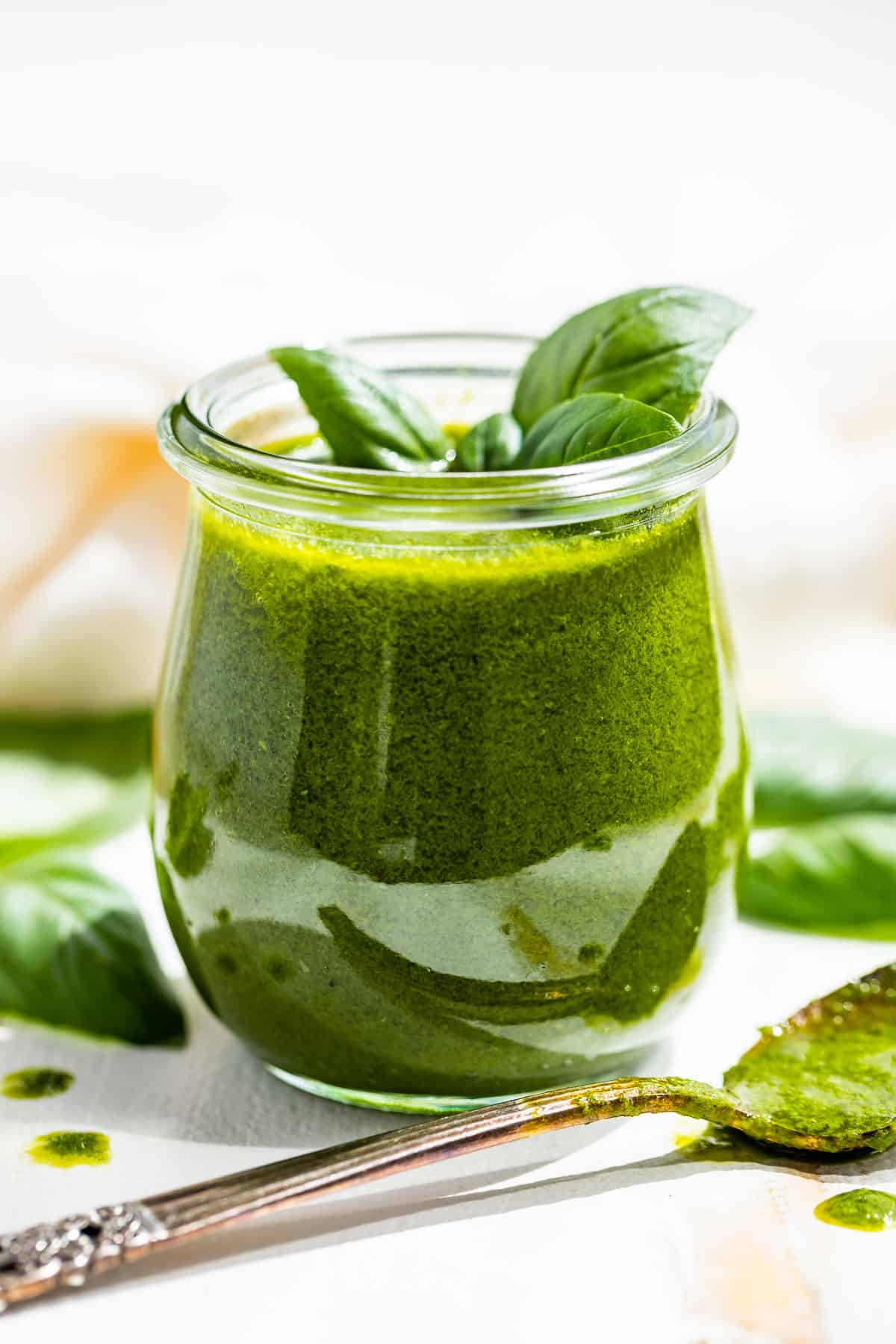 Side view of Basil Vinaigrette in a glass jar with a silver spoon full of dressing in front of the jar.