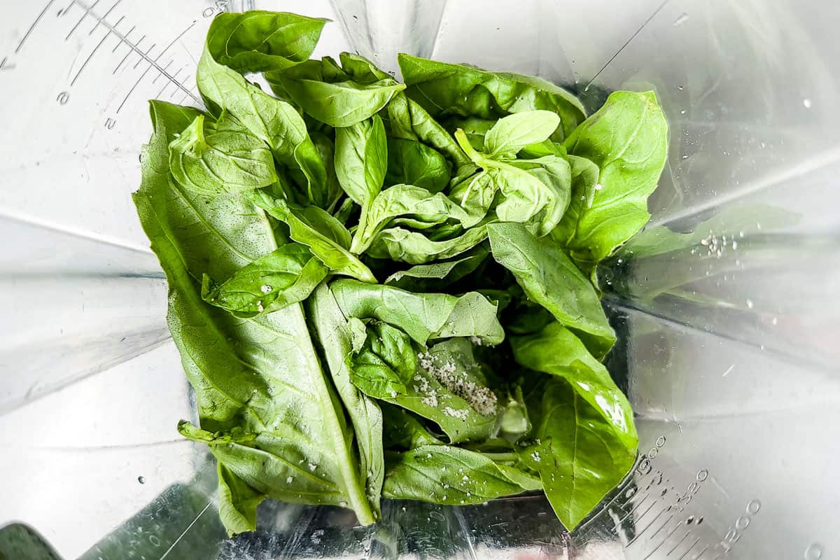 Adding the basil leaves on top of the vinaigrette ingredients in a blender container.