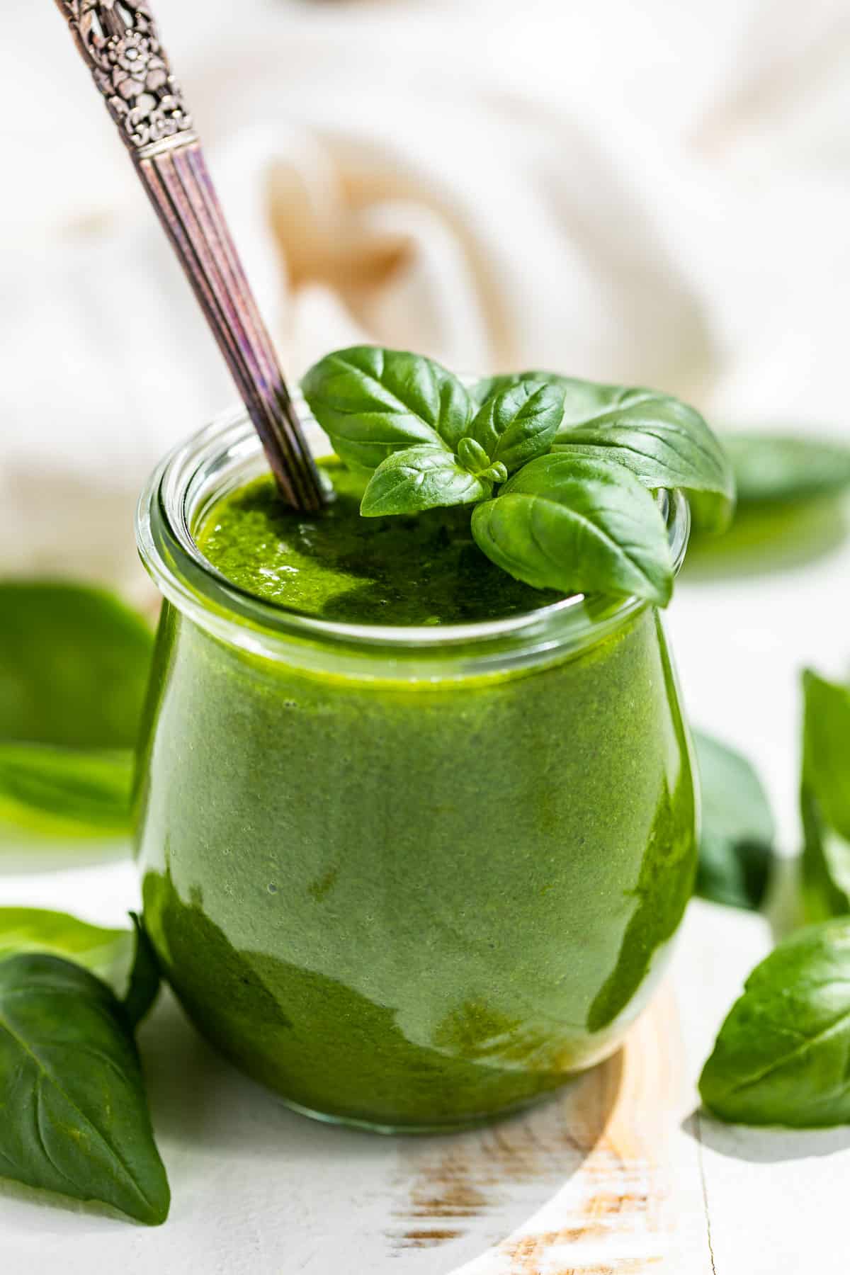 Side view of Basil Vinaigrette in a small glass tulip jar with a sprig of basil on top and basil around the container.