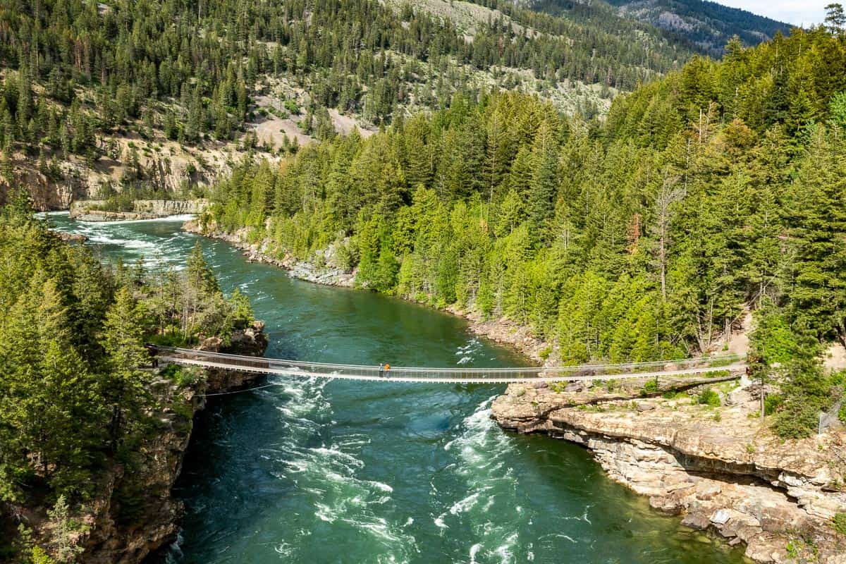 Drone view looking down at a man and woman standing on the swinging bridge suspended over the Kootenai river.