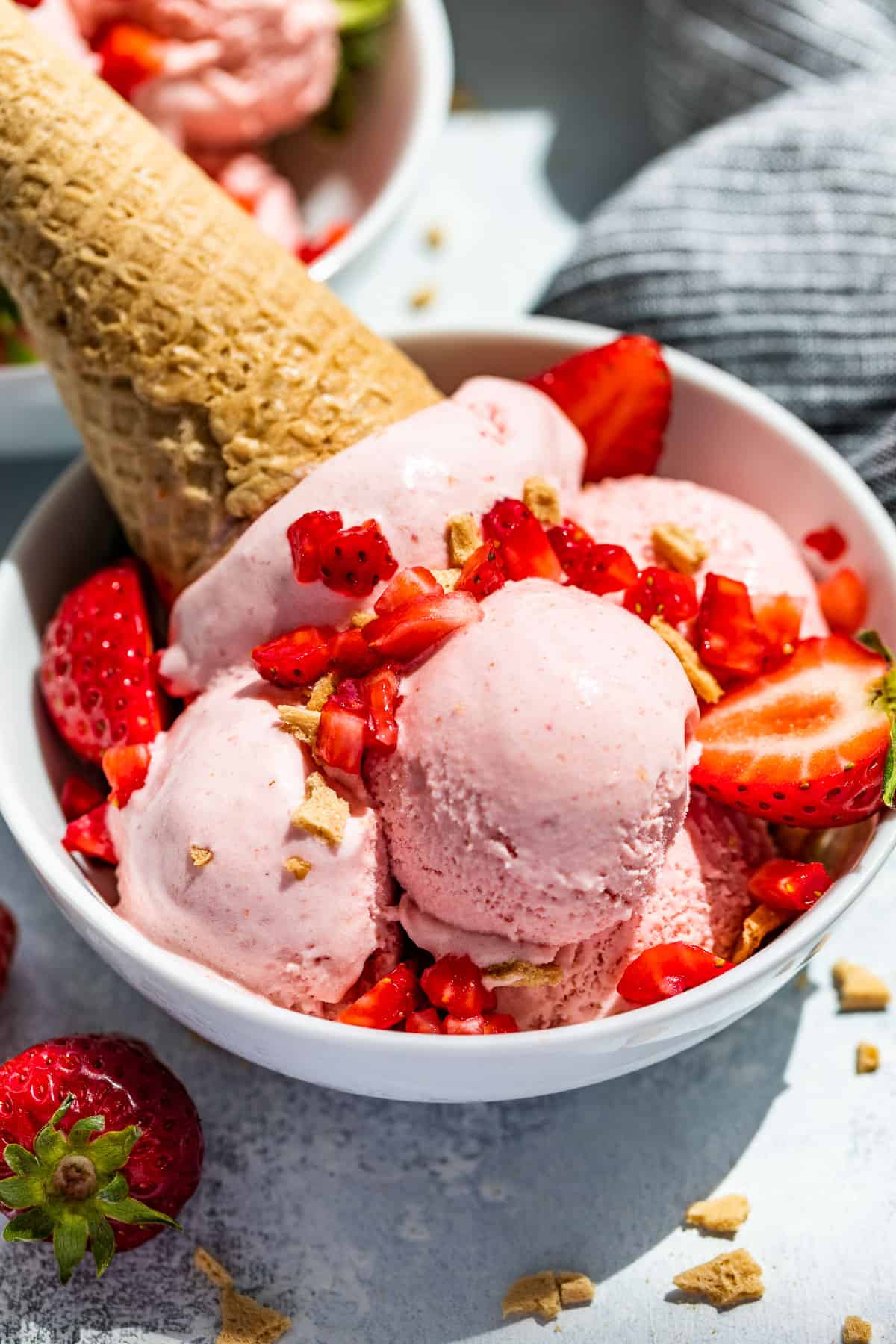 Side view of Strawberry Cheesecake Ice Cream scooped into a white bowl topped with strawberries and crumbled waffle cone.