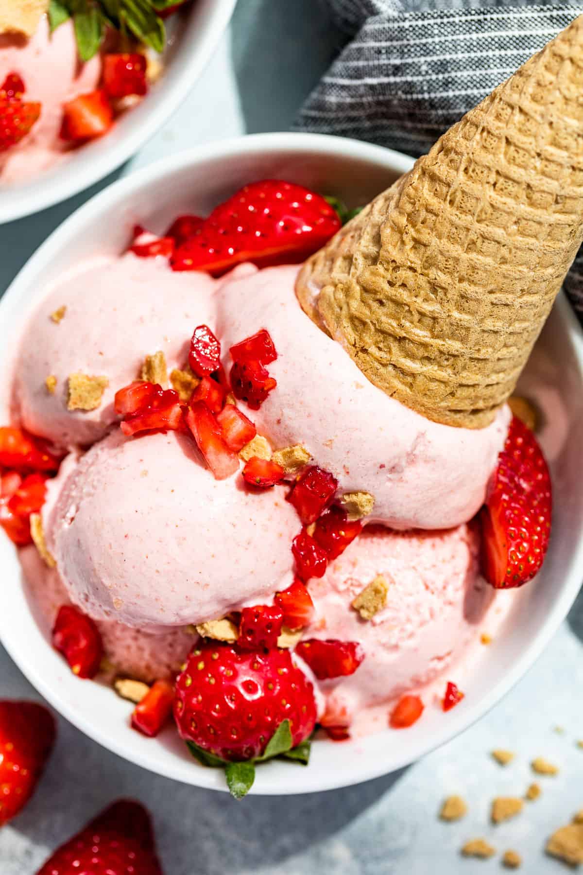 Close up straight down view of Strawberry Cheesecake Ice Cream scooped into a white bowl topped with fresh strawberries and crumbled waffle cone.