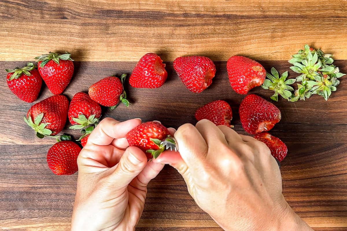 Hulling fresh strawberries on a wood cutting board.