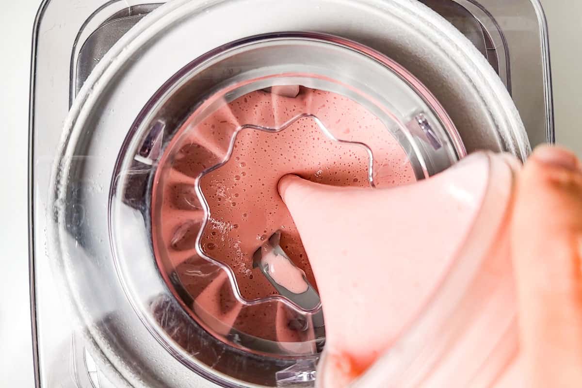 Adding the chilled strawberry ice cream base to an ice cream maker.