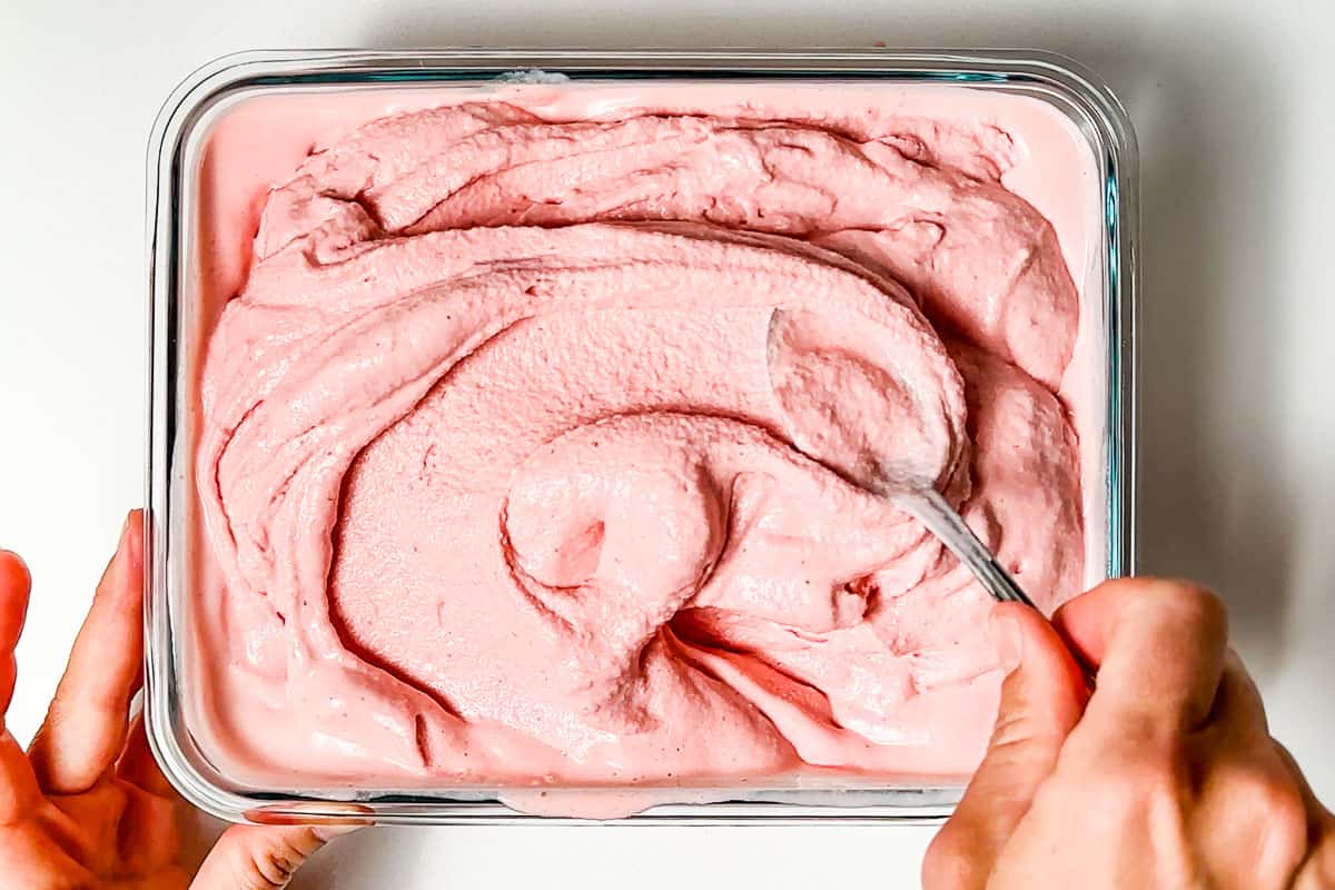 Evenly spreading the soft serve strawberry cheesecake ice cream into a freezer container.