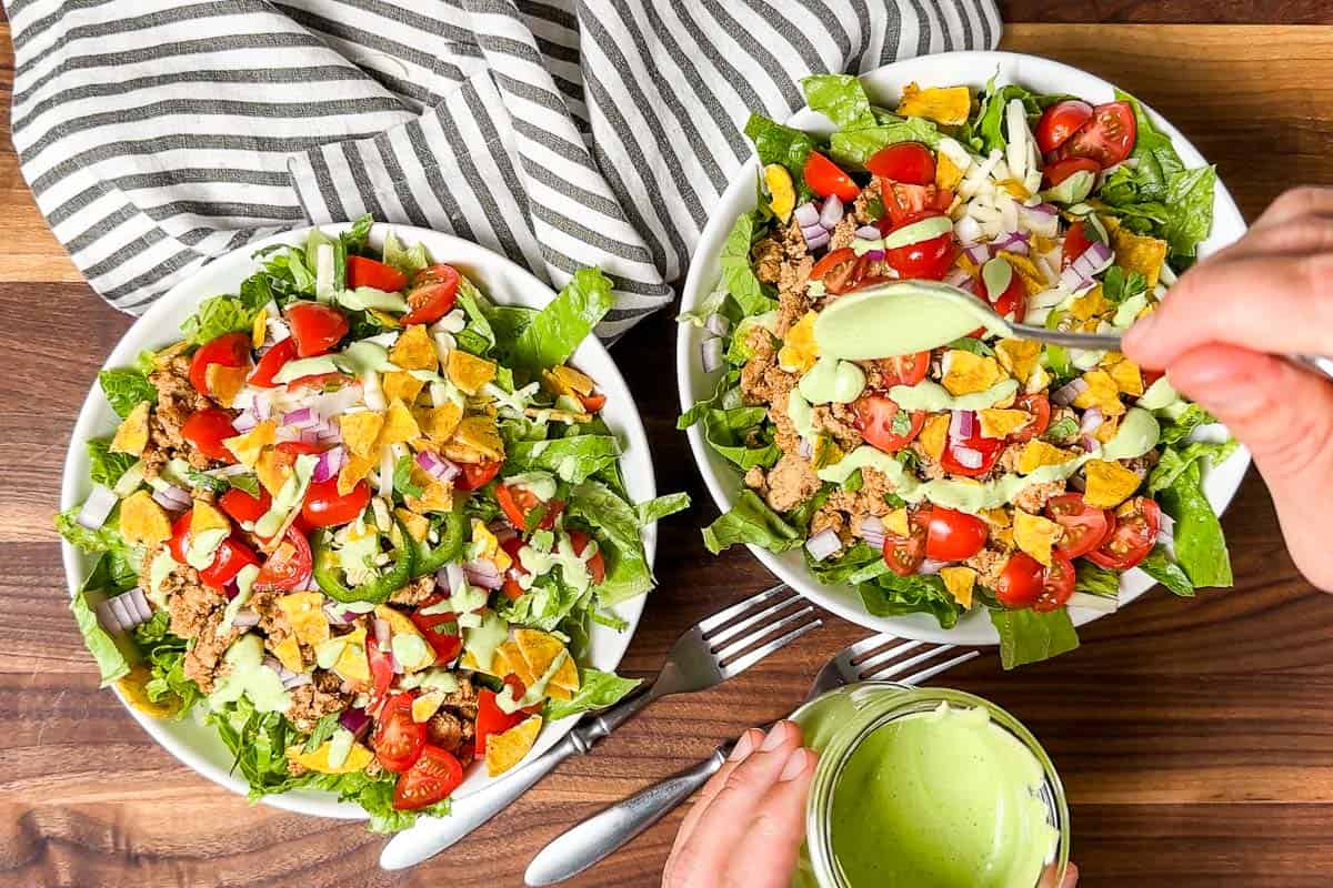 Drizzling the two bowls of taco salad with cilantro dressing.