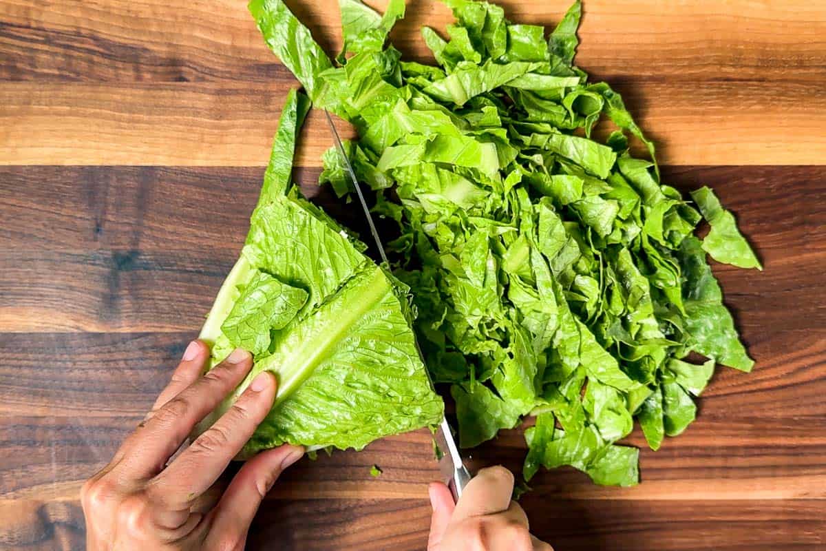 Chopping up a head of romaine on a wood cutting board.