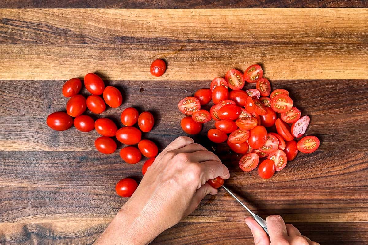 Cutting up cherry tomatoes on a wood cutting board.