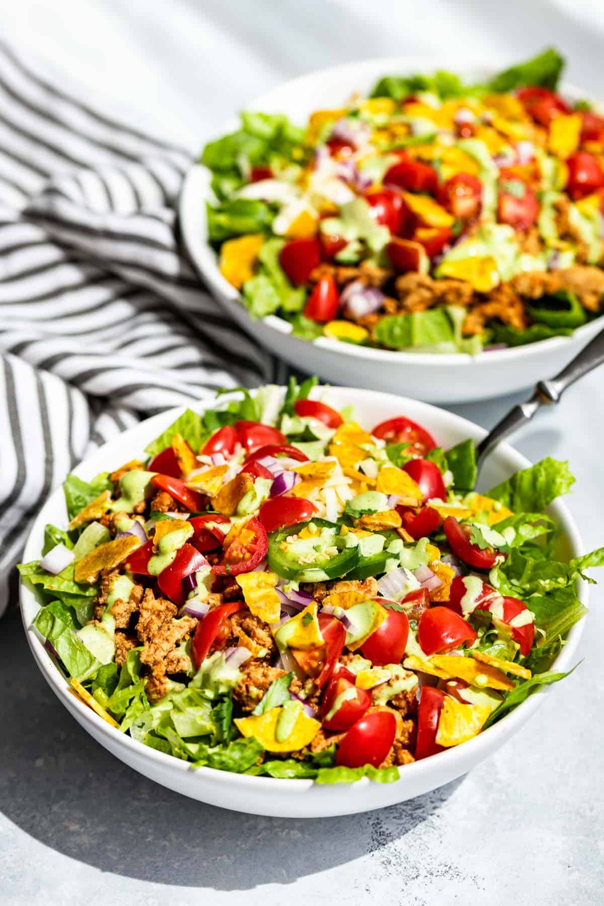 Side view of two white bowls of Turkey Taco Salad with a black and white striped linen in the background.