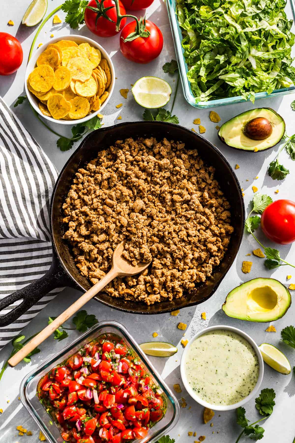 A skillet with turkey taco meat with plantain chips, romaine, tomatoes, avocado, and cilantro dressing on the side.