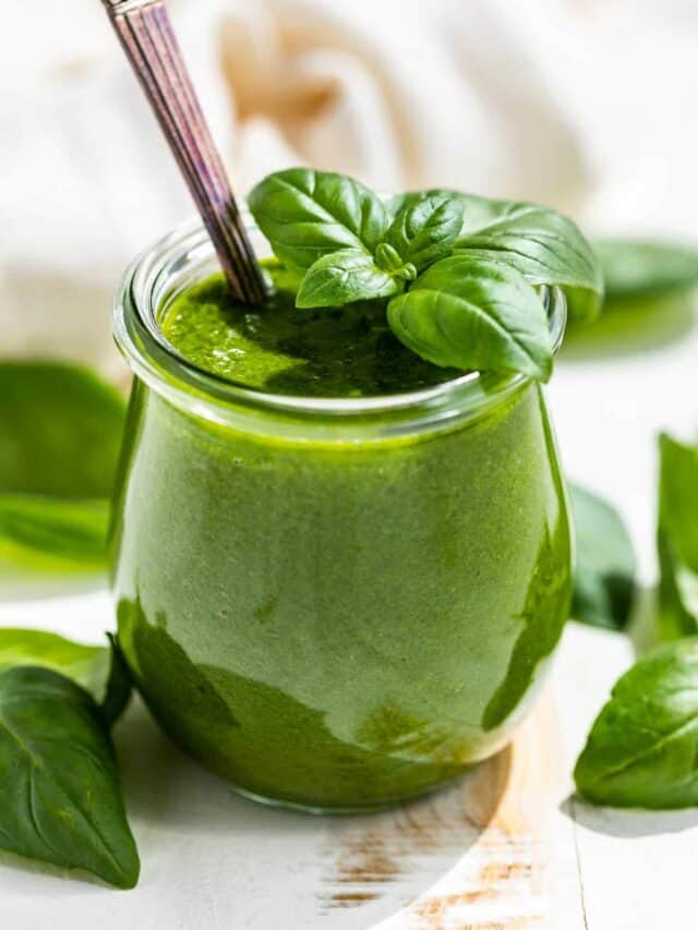 Side view of Basil Vinaigrette in a small glass tulip jar with a sprig of basil on top and basil around the container.